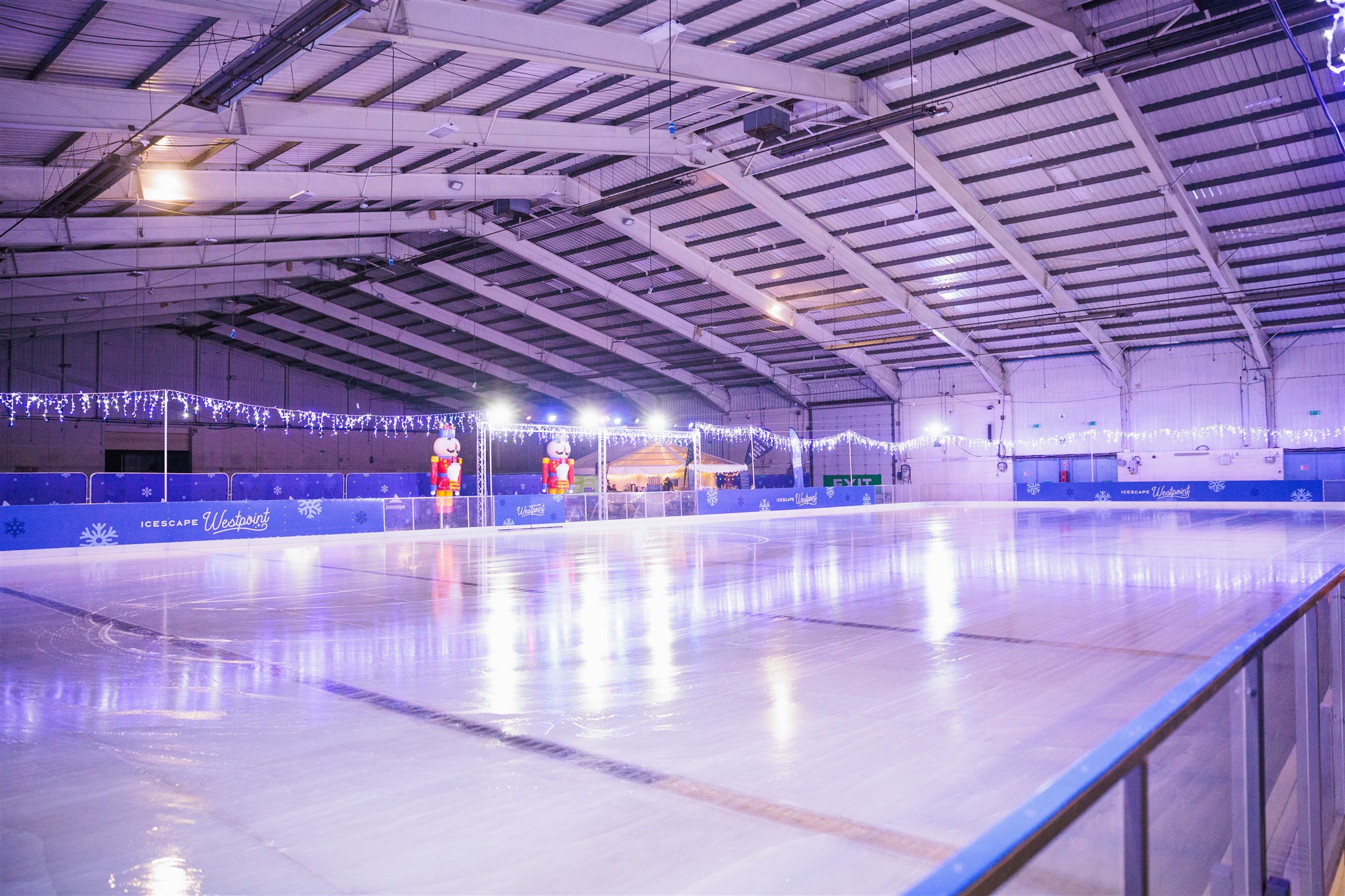 An empty real ice rink at Westpoint Arena. Two Nutcracker Soldiers and Christmas lights surround the ice rink which glistens in the vast arena. 