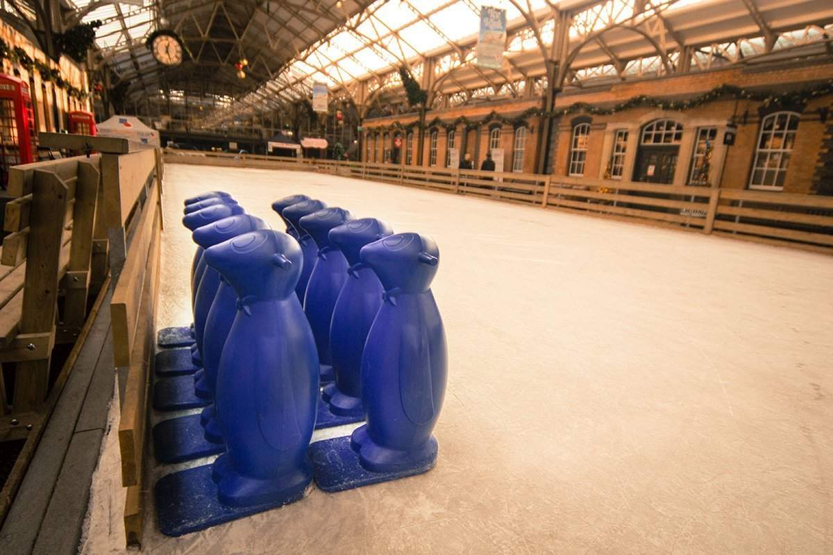 Two rows of blue penguin skates aid sitting on a real winter ice rink. 