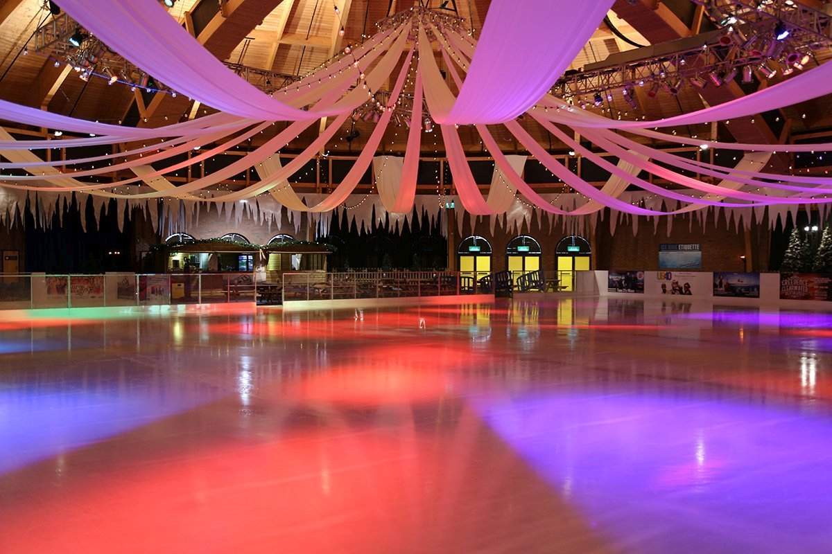 Covered winter ice rink at Bournemouth International Centre. The empty ice rink is lit up in colours with drapes hanging from the ceiling. 