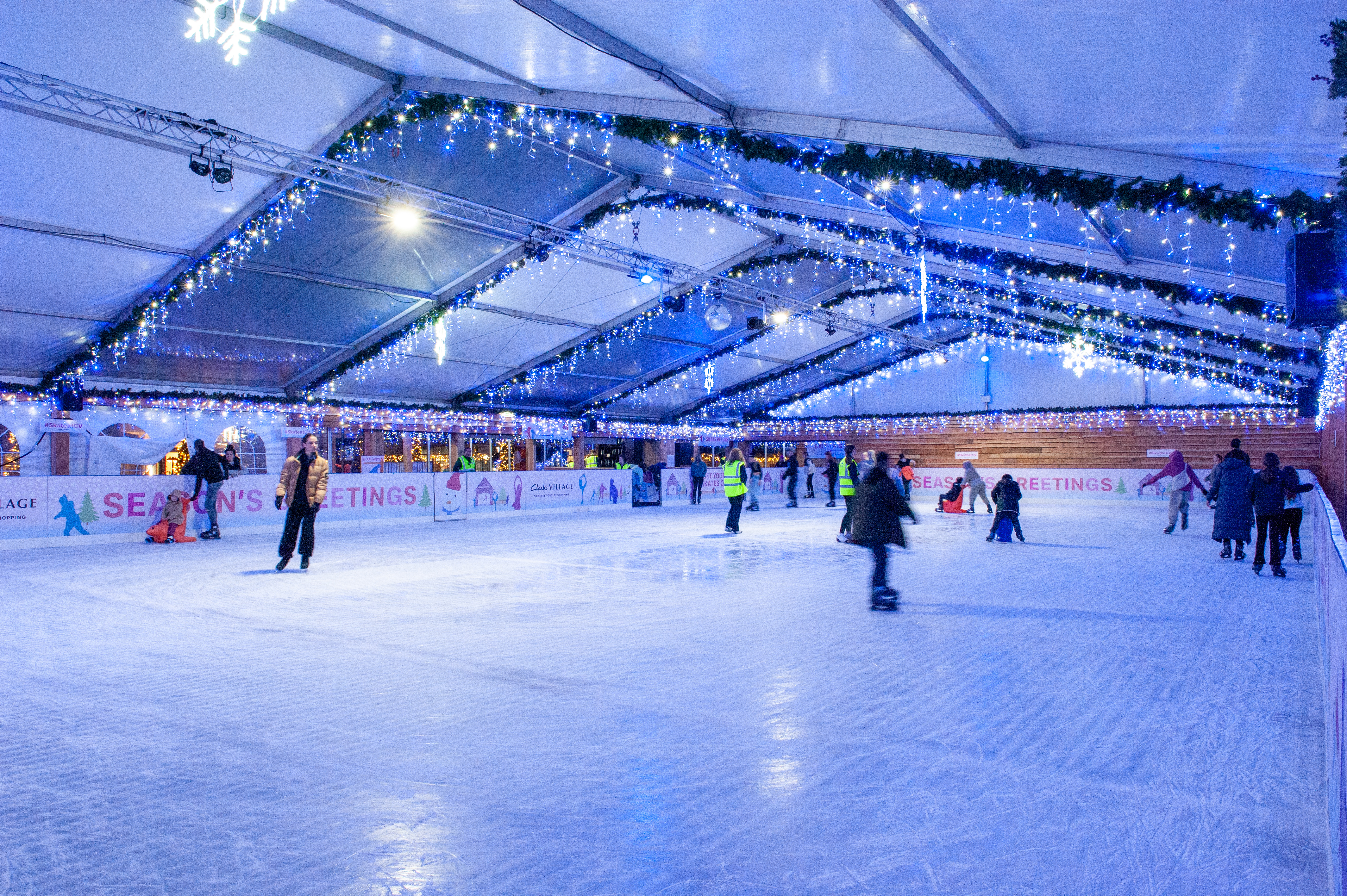 Clarks Village winter ice rink 2023 at night all lit up with skaters on the ice. 